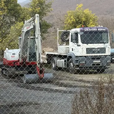 Retroexcavadora junto a camión cuba en trabajos de riego de obra. Maquinaria con operador cualificado y mantenimiento al día.
